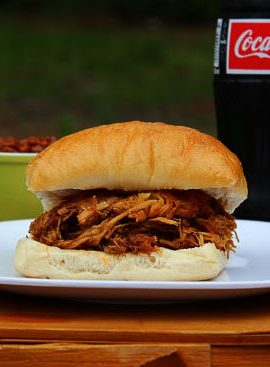 BBQ Pulled Pork Sandwich on top of picnic basket with a coca cola bottle in background.