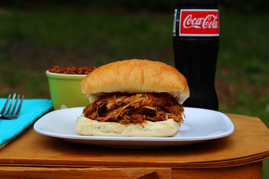 BBQ Pulled Pork Sandwich on top of picnic basket with a coca cola bottle in background.