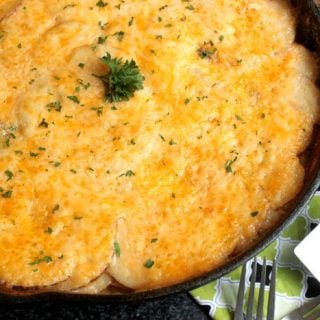 The Cheesy Skillet Au Gratin Potatoes are piled high in a cast iron skillet which means they can be cooked in the oven or in a covered grill