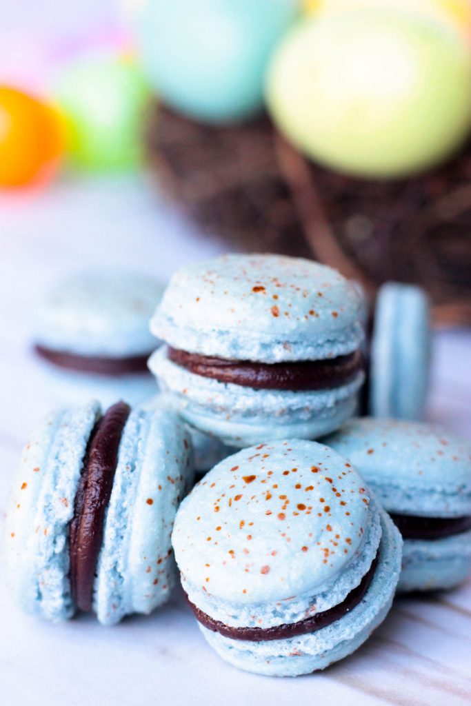 Robin Egg Macarons in a pile with Easter Eggs in the background