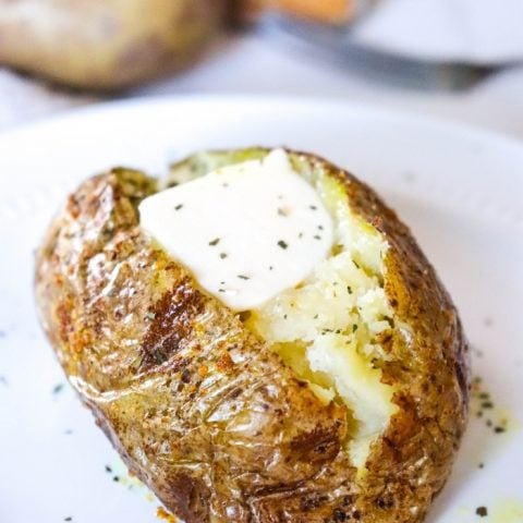 Baked Potato Cut open on white plate with butter and parsley