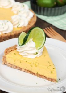 Slice of KEY LIME TART with whipped cream topping and lime zest on white plate (1)