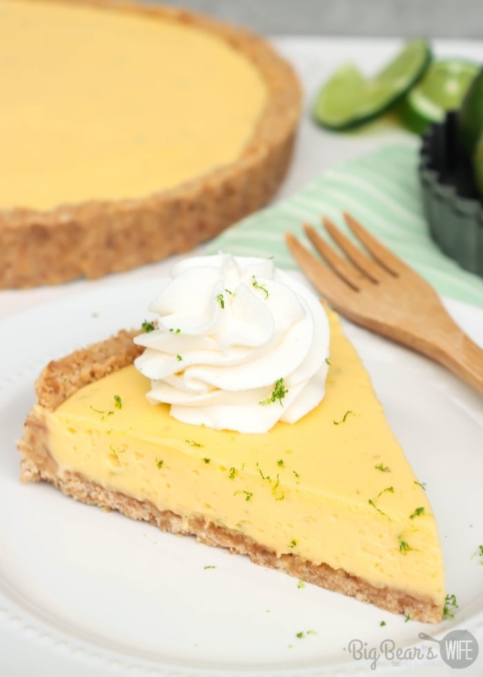 Slice of KEY LIME TART with whipped cream topping and lime zest on white plate