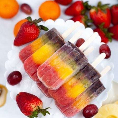 Rainbow Popsicles on ice in a white bowl surrounded by fruit