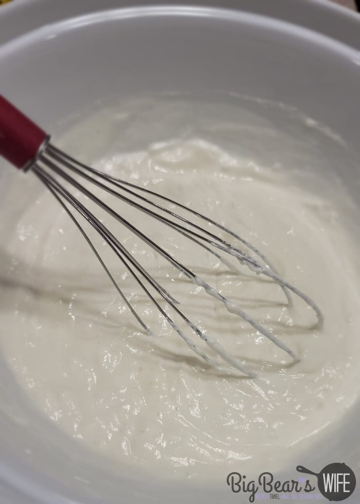 Pineapple juice and whipped topping being whisked in a white bowl