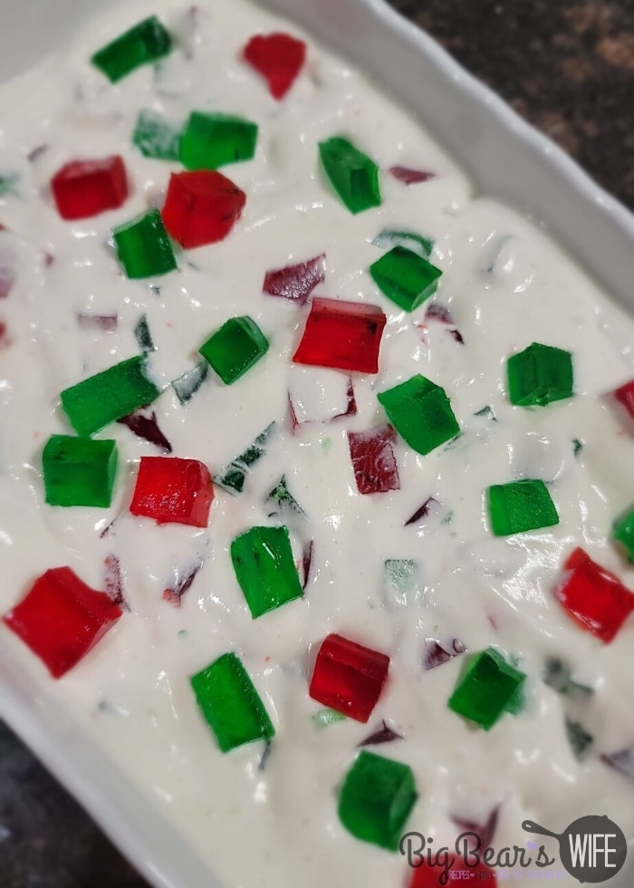 Red and Green Jell-O squares in whipped topping in a white casserole dish topped with more red and green Jell-O squares