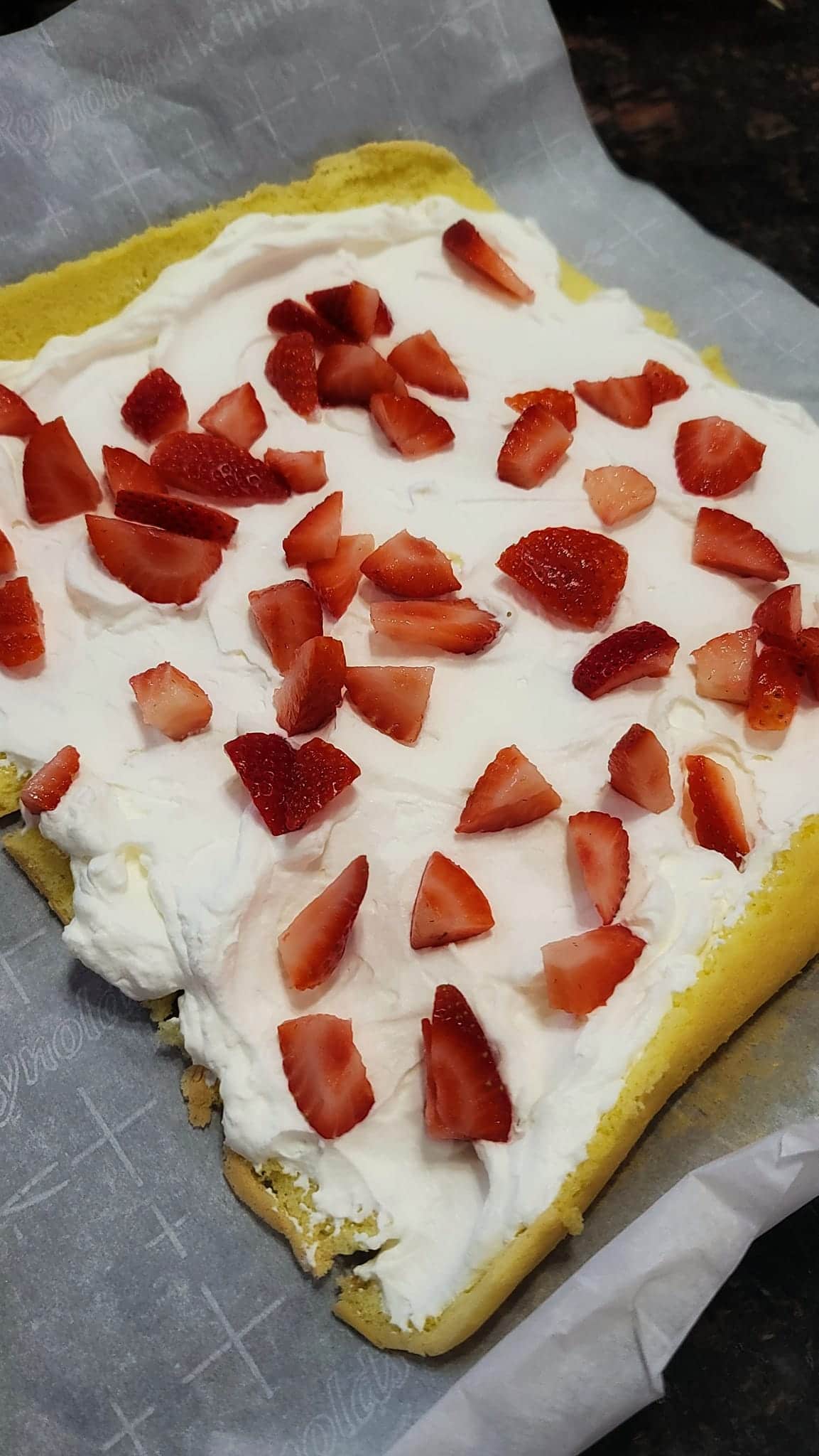 chopped strawberries on whipped cream on yellow sponge cake for cake roll