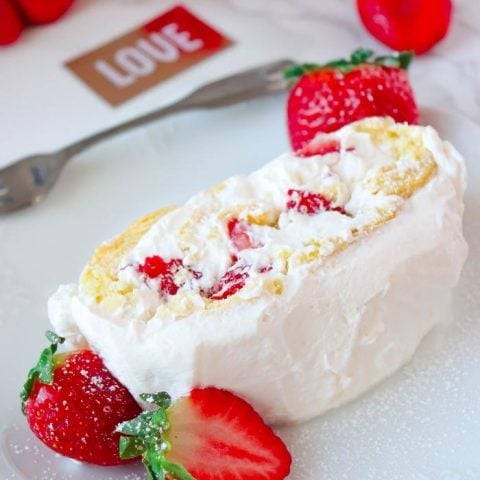 Slice of STRAWBERRY SHORTCAKE ROLL on white plate with LOVE in background and strawberries