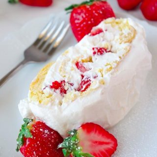 Slice of STRAWBERRY SHORTCAKE ROLL on white plate in background and strawberries