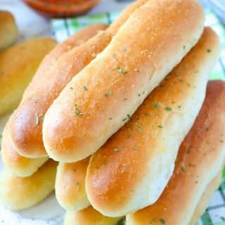 A stack of COPYCAT OLIVE GARDEN BREADSTICKs with pizza sauce in the background