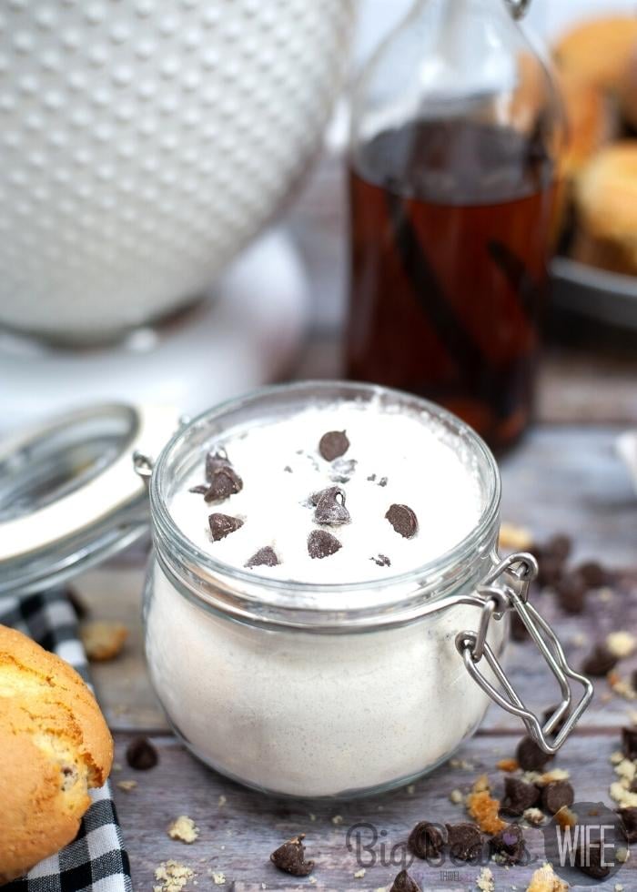 DRY CHOCOLATE CHIP MUFFIN MIX in a glass jar with chocolate chips scattered around and a white bowl and vanilla extract in the background