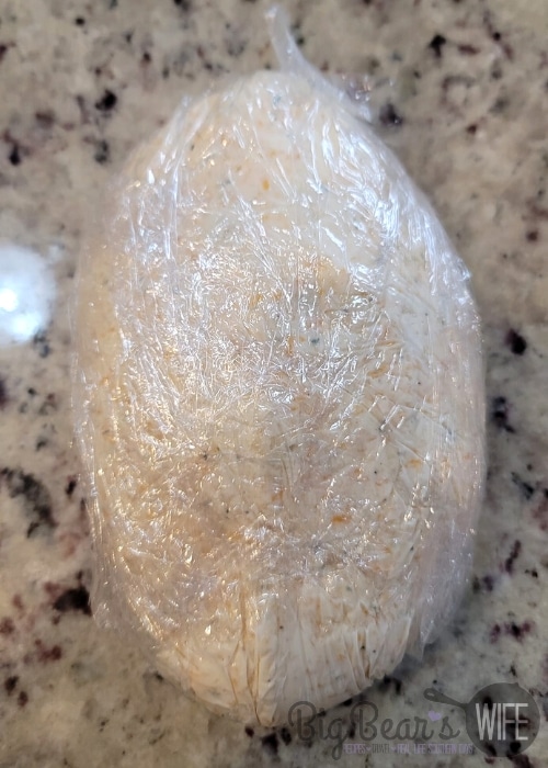 cheeseball mixture shaped into a football and wrapped in plastic wrap