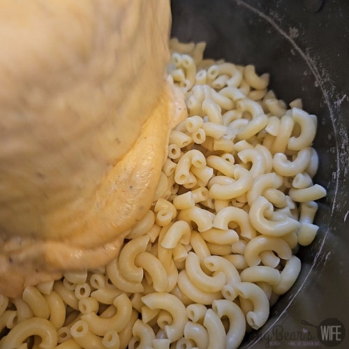 pouring cheese sauce over pasta