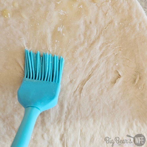 brushing butter on spread out cinnamon roll dough